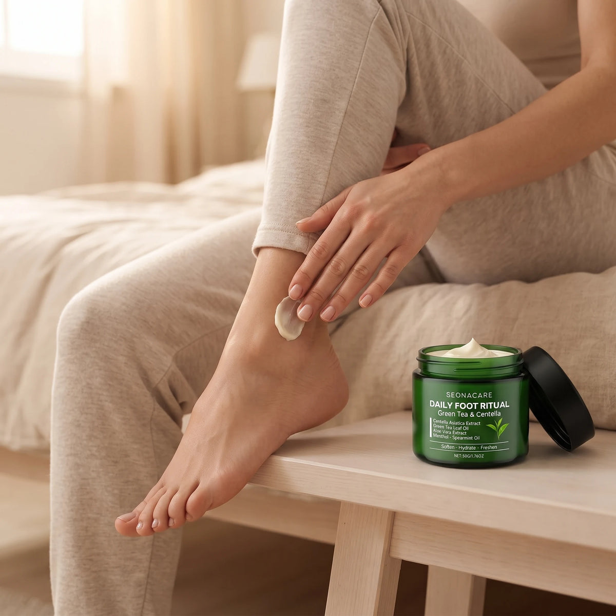 A woman smoothing the cream onto her heel while seated, the open jar beside her